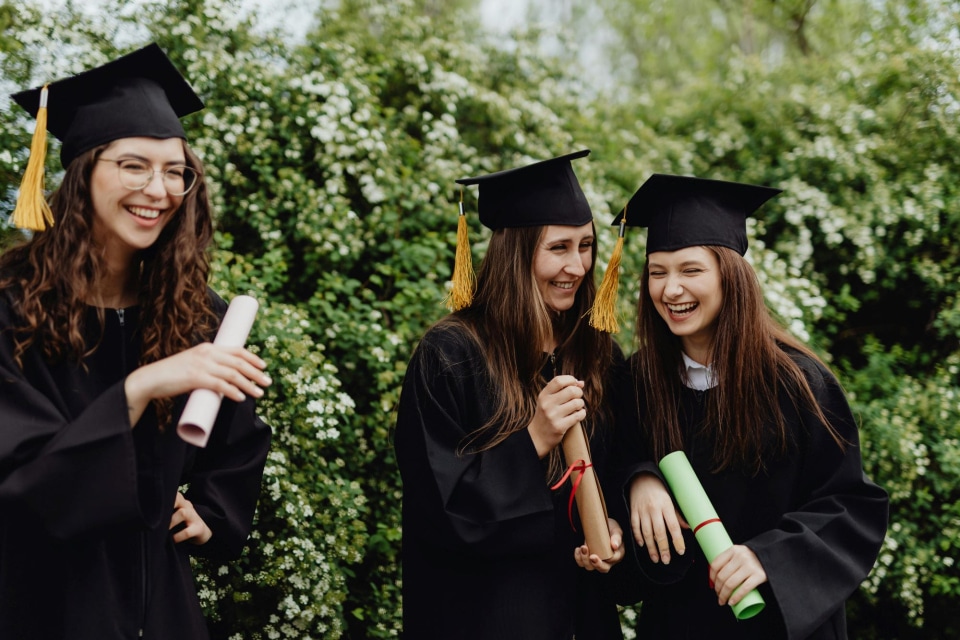 Three graduates in caps and gowns laughing together.